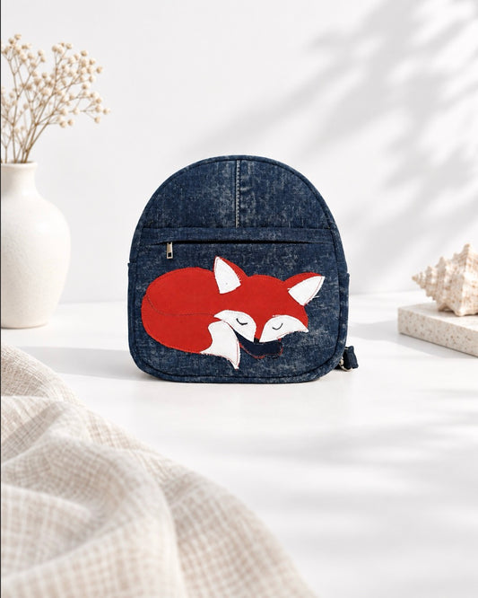 A small dark blue denim backpack with a red fox applique on the front