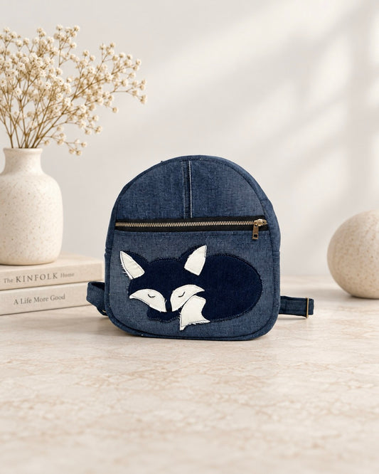 A small denim backpack with a fox face applique on the front